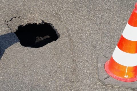 Aufgebrochene Asphaltdecke mit einem tiefen Schlagloch in der Fahrbahn. 
