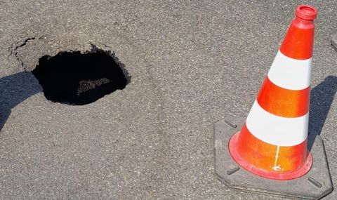 Aufgebrochene Asphaltdecke mit einem tiefen Schlagloch in der Fahrbahn. 