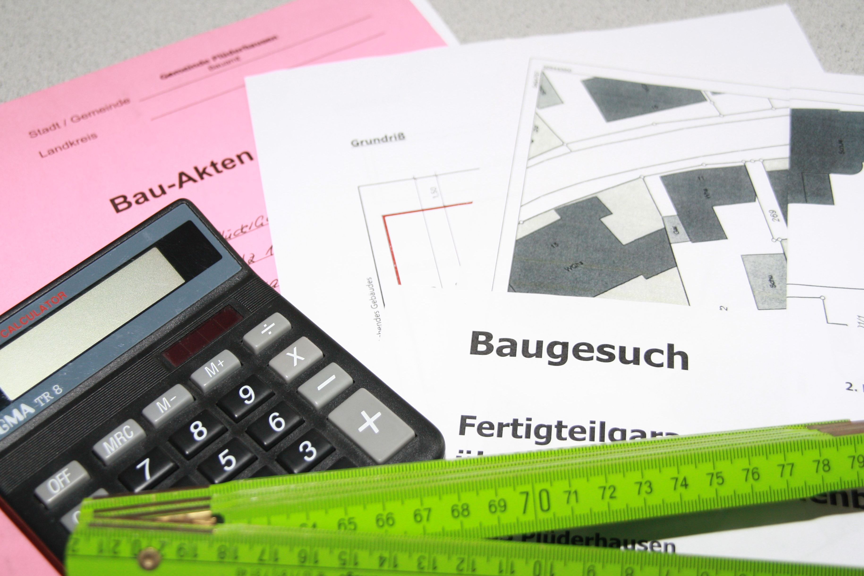 Ein Taschenrechner und ein Meterstab liegen auf einer Bauakte