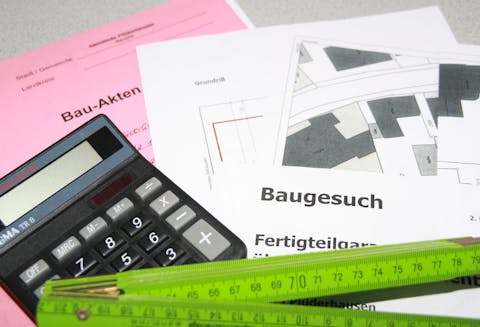 auf einem Tisch liegen Bauakten, ein Taschenrechner sowie ein Meterstab