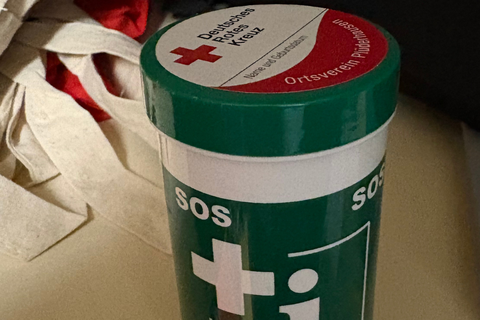 Eine Notfalldose in grün mit weißem Aufdruck SOS, Kreuz, ...