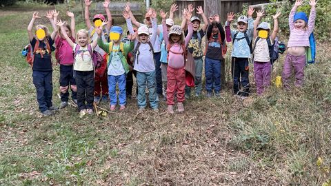 Die Kinder des Waldkindergarten vor der Hütte auf dem Hohbergkopf mit nach oben gestreckten Armen