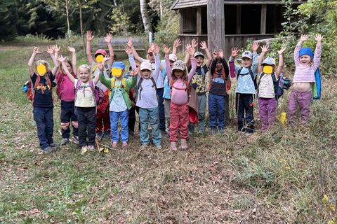 Die Kinder des Waldkindergarten vor der Hütte auf dem Hohbergkopf mit nach oben gestreckten Armen