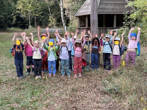 Die Kinder des Waldkindergarten vor der Hütte auf dem Hohbergkopf mit nach oben gestreckten Armen