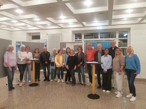 Das Bild zeigt Bürgerinnen und Bürger der Gemeinde Plüderhausen mit Mitarbeitern der Gemeindeverwaltung und unserem Moderator Herrn Wolfgang Klenk im Foyer der Staufenhalle, die sich vor Pinnwänden positioniert haben, welche die ersten Ergebnisse des Wo