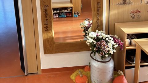 Spiegel an der Wand mit Holzrahmen, Sprüchen im Rahmen und im Vordergrund eine herbstlich geschmückte Vase und Kürbisse