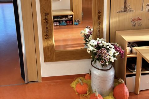 Spiegel an der Wand mit Holzrahmen, Sprüchen im Rahmen und im Vordergrund eine herbstlich geschmückte Vase und Kürbisse