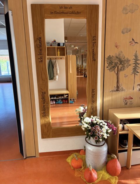 Spiegel an der Wand mit Holzrahmen, Sprüchen im Rahmen und im Vordergrund eine herbstlich geschmückte Vase und Kürbisse