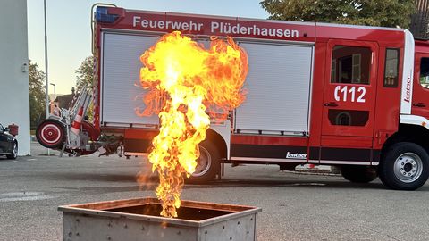 Feuerlöschertrainer: Metallgestell mit Gasflamme, im Hindergrund ein Feuerwehrauto
