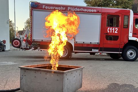 Feuerlöschertrainer: Metallgestell mit Gasflamme, im Hindergrund ein Feuerwehrauto