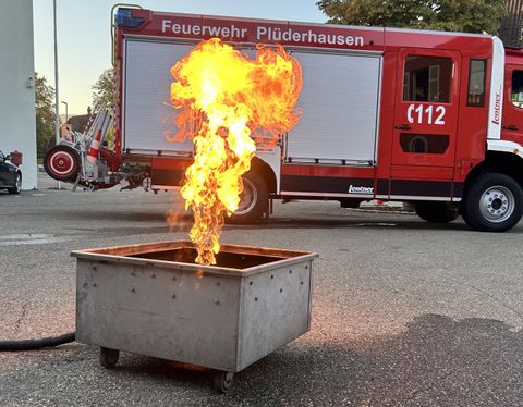 Feuerlöschertrainer: Metallgestell mit Gasflamme, im Hindergrund ein Feuerwehrauto