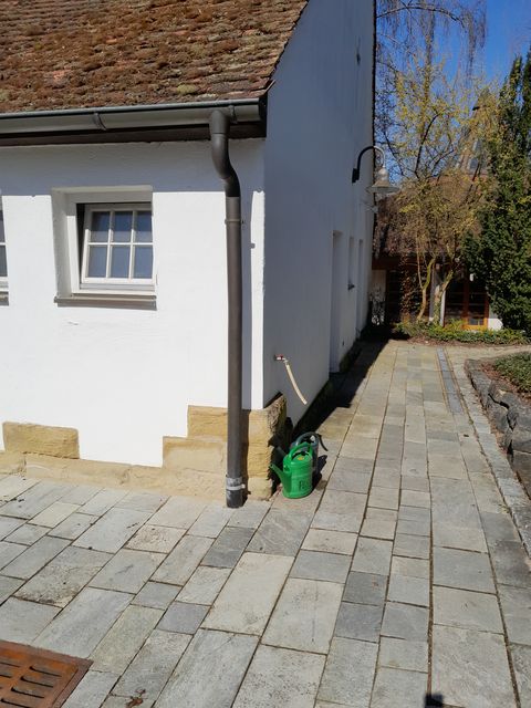 Das Bild zeigt eine Giesskanne am Wasserhahn des WC Gebäudes auf dem Friedhof.