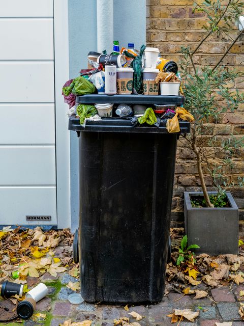 Ein überfüllter Müllcontainer mit Verpackungen und Essensresten steht vor einem Haus.